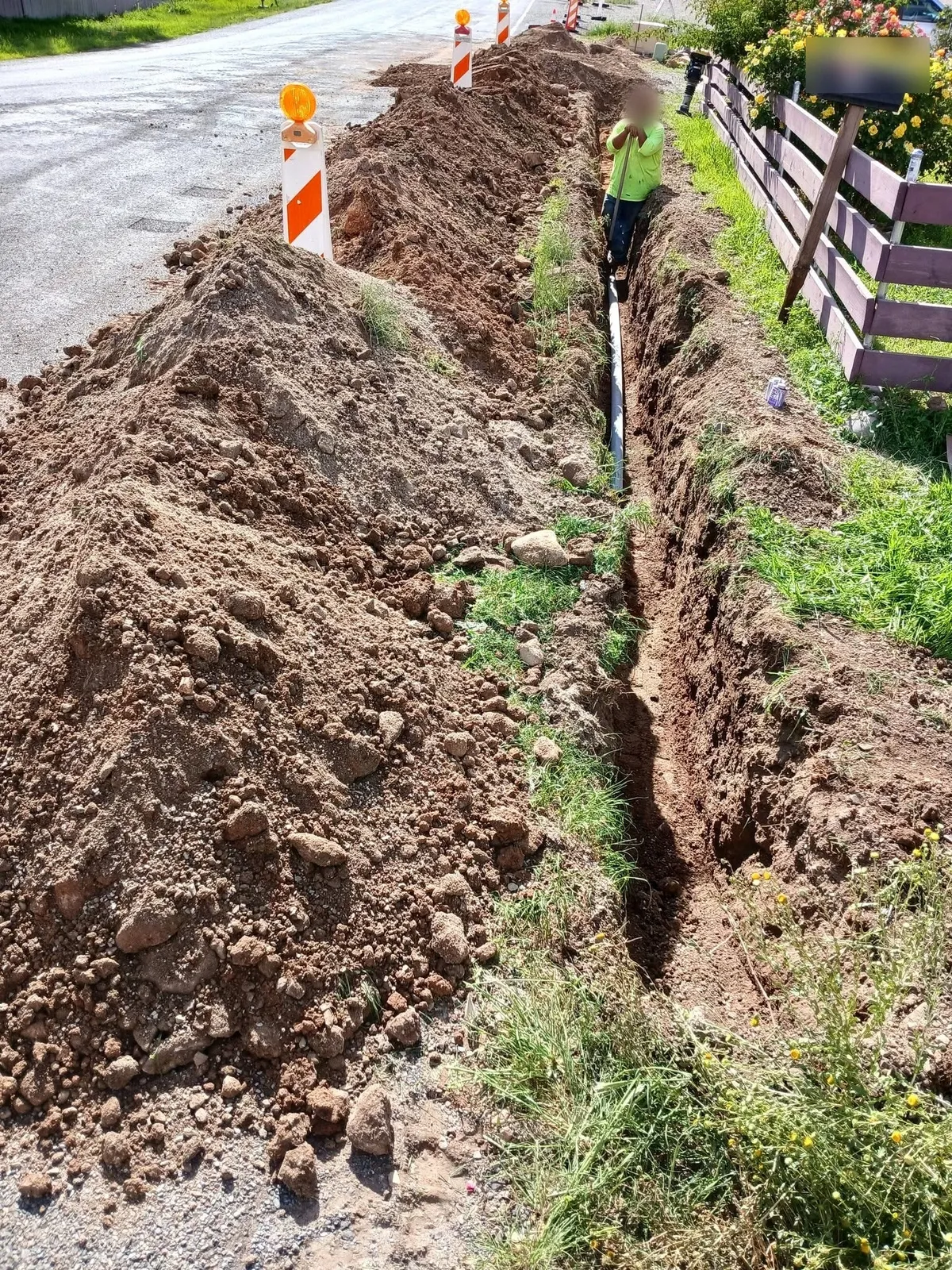 Utility trench dug along a roadside with barricades